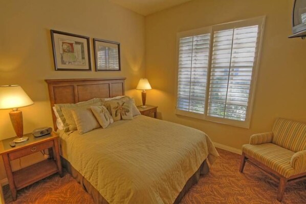 A bedroom with a bed, two bedside tables, a chair, and a window with blinds.