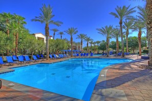 A swimming pool with blue water, surrounded by palm trees and blue lounge chairs.