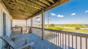 Um deck de madeira com mesa e cadeiras, com vista para uma estrada e vegetação.