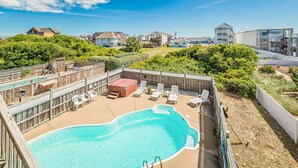 Área de piscina com espreguiçadeiras e banheira de hidromassagem, cercada por uma cerca de madeira e vegetação.