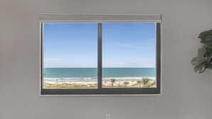 Een slaapkamer met een groot raam dat uitkijkt op een strand.