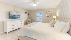 A bedroom with a bed, a ceiling fan, a TV, a dresser, a window, and a mirror. - Seaside Luxury Private Balcony, Breathtaking Views & Steps to the Sand (Cape Canaveral)