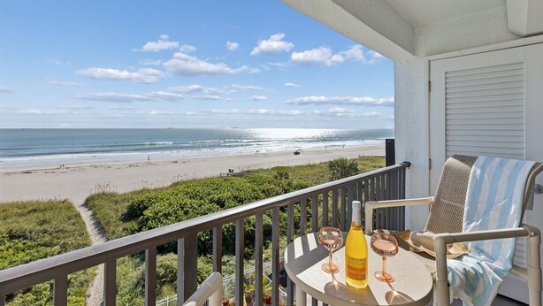 Een balkon met uitzicht op het strand, een tafel met een fles en glazen, en een stoel met een gestreepte handdoek.