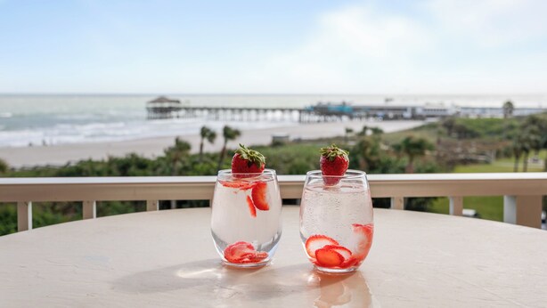 Two glasses of water with strawberries on a table with a view of the beach and pier. - Penthouse Paradise Steps to Pier with Ocean Views & Private Beach Access (Cocoa Beach)