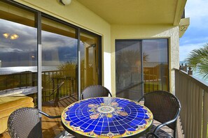 A balcony with a round table and chairs, a view of the ocean, and a palm tree. - Land's End 303 building 6 Gorgeous 3rd floor remodeled beach front condo! (Treasure Island)