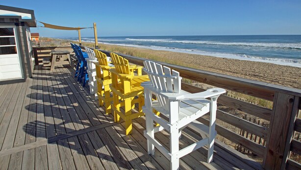 Een houten terras met stoelen en een tafel met uitzicht op het strand.