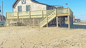 Een houten gebouw met een trap naar een terras, gelegen op een zandstrand.