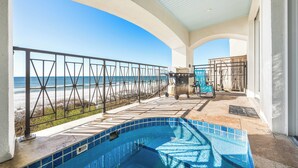 Zona de piscina con vistas a la playa y al océano, una parrilla y un porche cubierto.