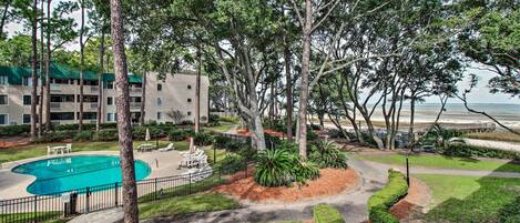 A pool area with a fenced deck, surrounded by trees and a building with balconies.