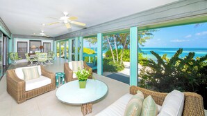 A spacious outdoor lounge area with wicker furniture, a round glass table, and a view of the ocean. - Fingertip: Gorgeous Waterfront Villa in Cayman Kai w/Private Beachfront! (Grand Cayman)
