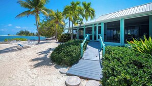 A beachfront property with a wooden deck leading to a building with large windows. - Fingertip: Gorgeous Waterfront Villa in Cayman Kai w/Private Beachfront! (Grand Cayman)