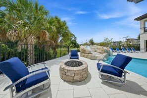 A poolside area with lounge chairs, a fire pit, and a pool with a water slide.