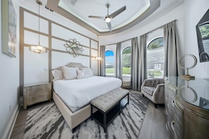 A bedroom with a large bed, a ceiling fan, a desk, and a chair.