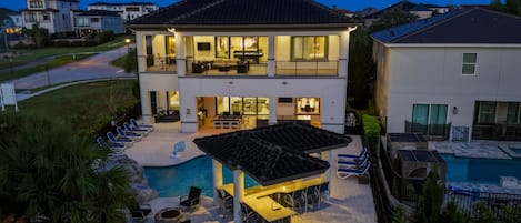 Una casa de dos pisos con piscina, mobiliario exterior y un patio bien iluminado.