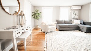 A modern living room with a white desk, a grey sofa, a white armchair, a large mirror, and a potted plant. - PORTLAND PENINSULA-SPACIOUS WALKABLE EAST END SPOT (Portland)