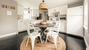 A modern kitchen with white cabinets, a round dining table with white chairs, a woven pendant light, and a black tiled floor. - PORTLAND PENINSULA-SPACIOUS WALKABLE EAST END SPOT (Portland)