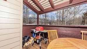 Un espacio al aire libre techado con una mesa y sillas de madera, una parrilla y vistas a árboles y montañas.