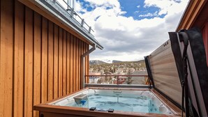 Une terrasse en bois avec un jacuzzi et une vue sur la ville et les montagnes.