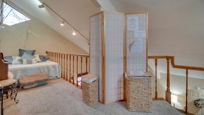 Un dormitorio con una cama, un banco de madera, un cesto de basura pequeño y un separador decorativo.