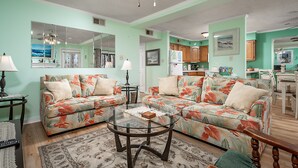 A living room with two floral sofas, a glass coffee table, and a wooden dining table. - Peaceful Bay Side Retreat with Large Pool perfect for a family vacation (Ocean City)