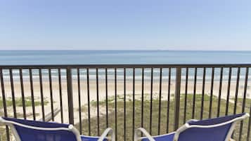 A balcony with two blue chairs facing a beach.