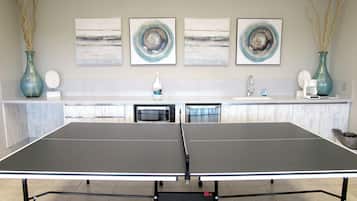 A ping pong table with a TIGA logo, a kitchen area with a sink, and three abstract paintings on the wall.