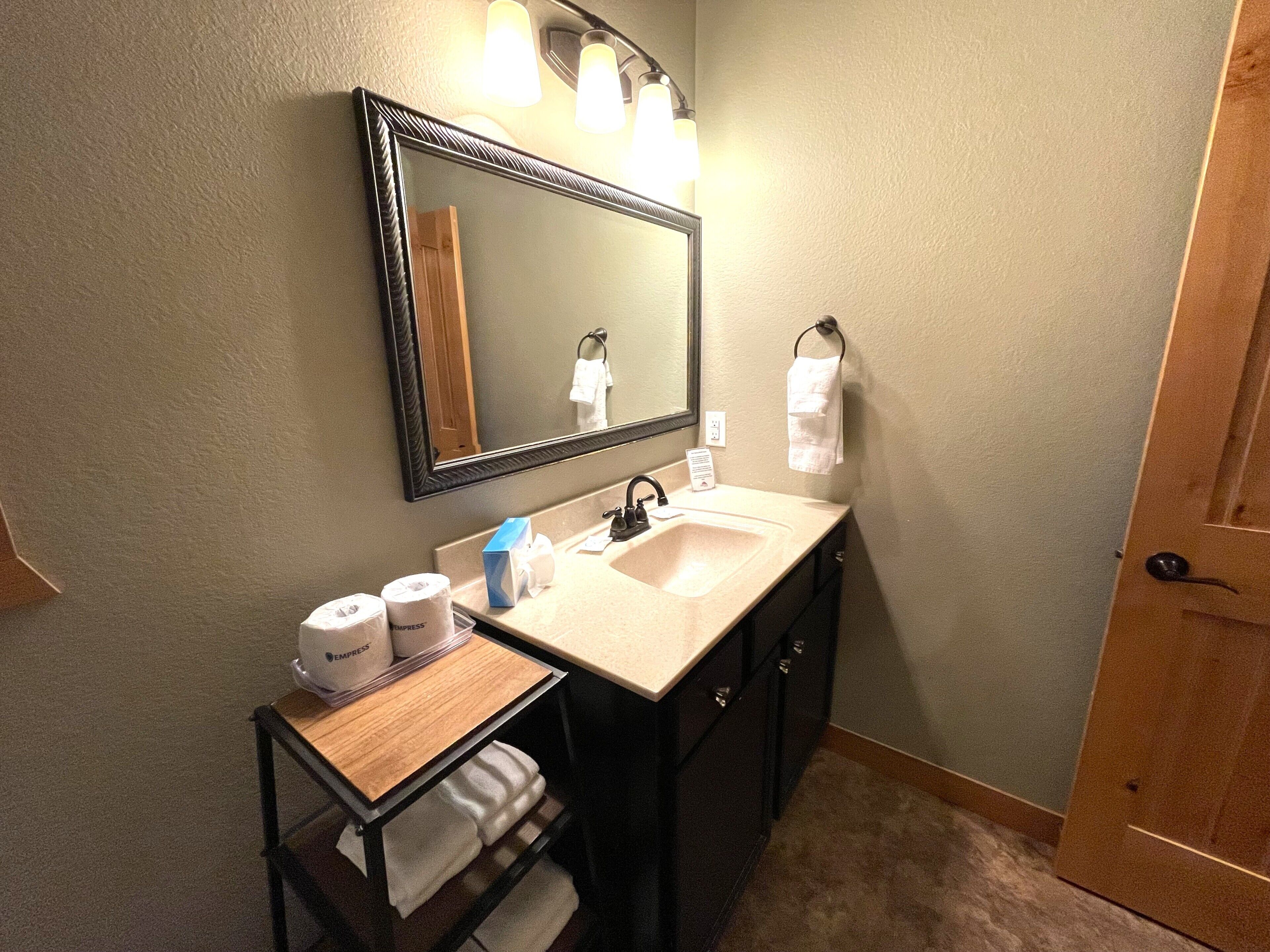 Une salle de bain équipée d’un lavabo, d’un miroir, d’un porte-serviettes et d’une petite étagère où sont rangés les articles de toilette.