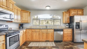 A kitchen with wooden cabinets, stainless steel appliances, a large window, and a view of trees. - Secluded Boulder House - Next to National Forests! (Boulder)