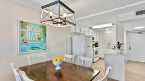 A modern kitchen with white cabinets, a central island, and a dining area with a wooden table and white chairs.