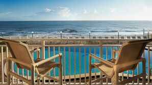 A poolside view with two wicker chairs and a clear view of the ocean.