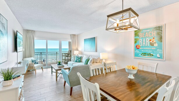 A spacious living area with a dining table, white chairs, and a view of the ocean.