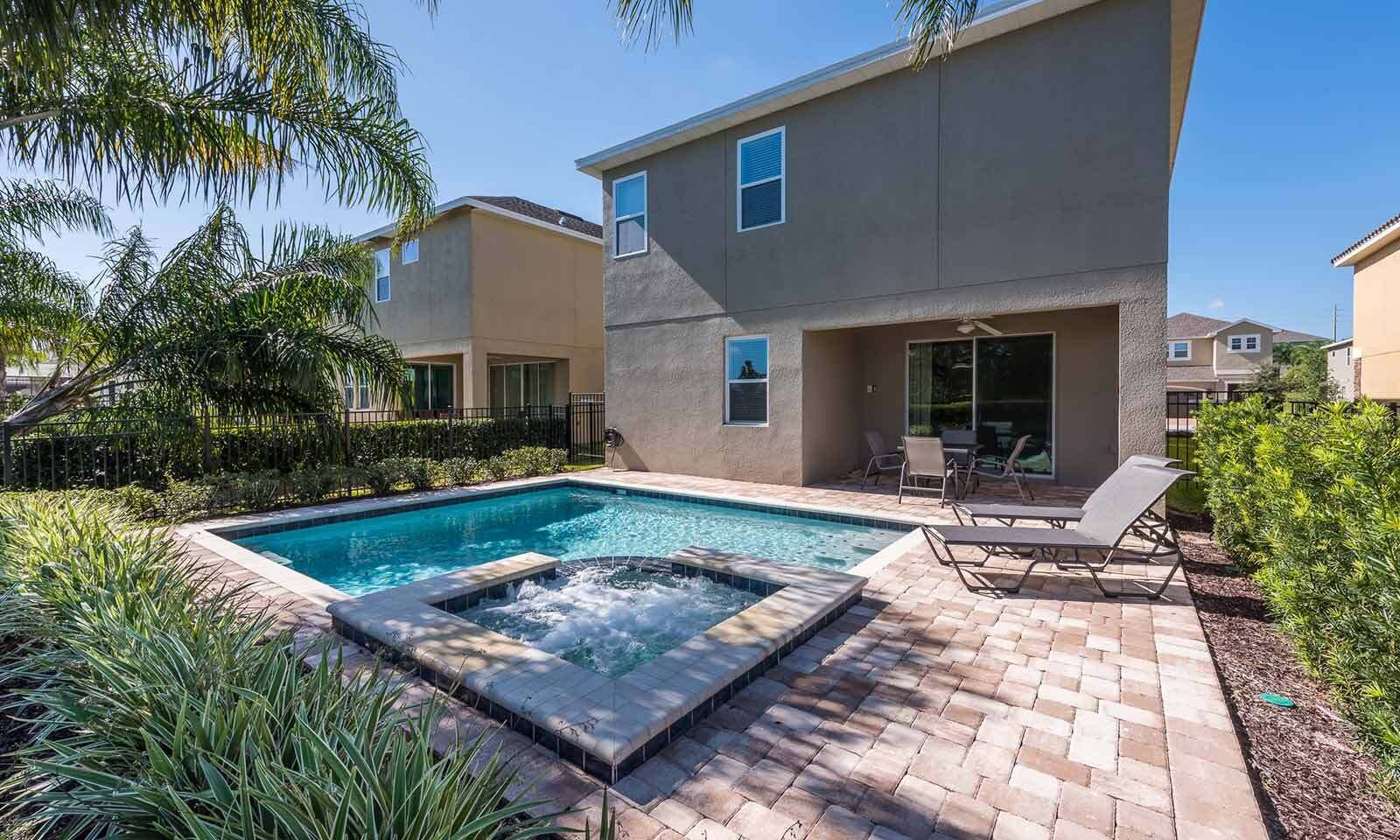 A modern residential building with a swimming pool and hot tub, surrounded by lush greenery.
