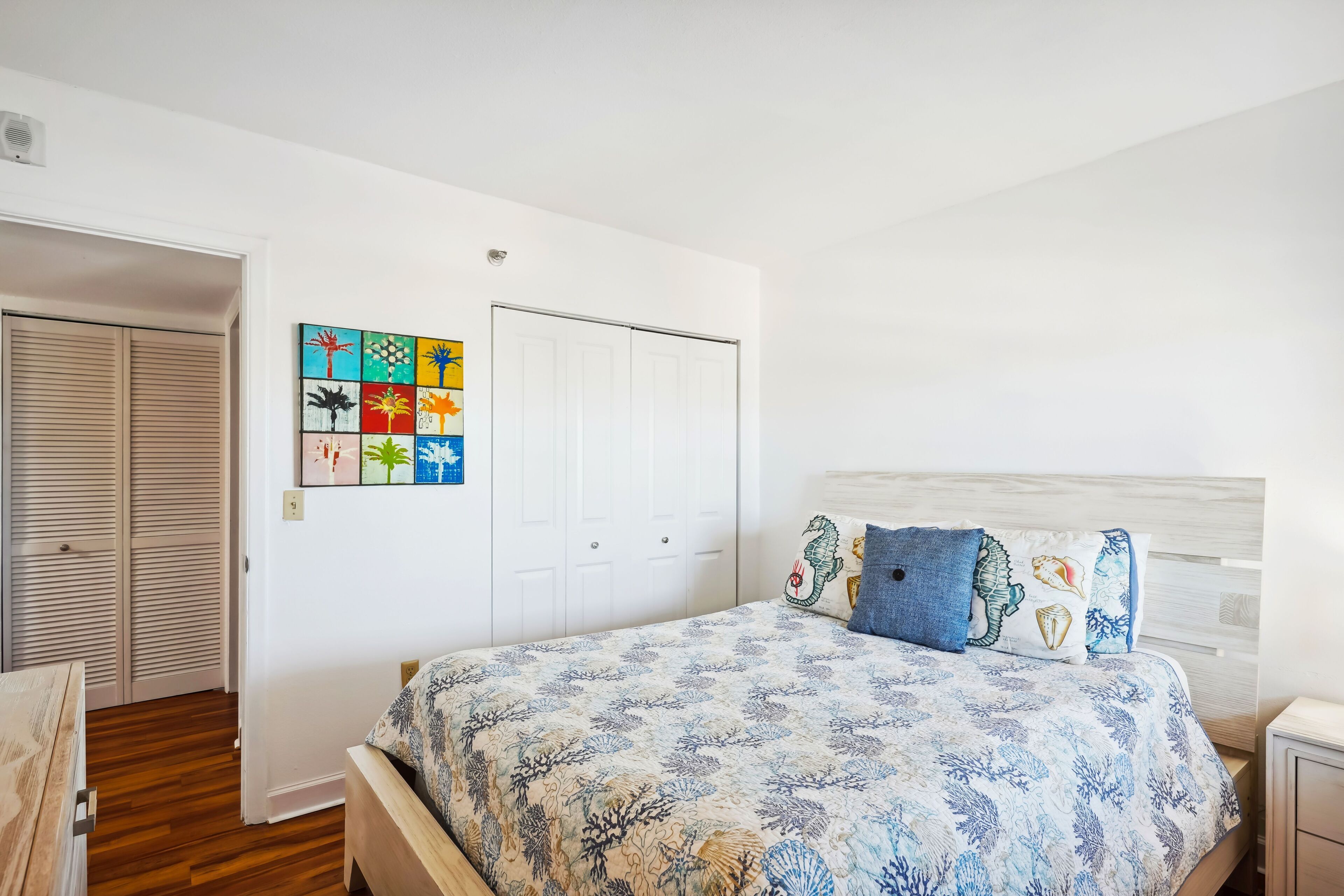 Un dormitorio con cama, armario y una pared decorada con obras de arte coloridas.