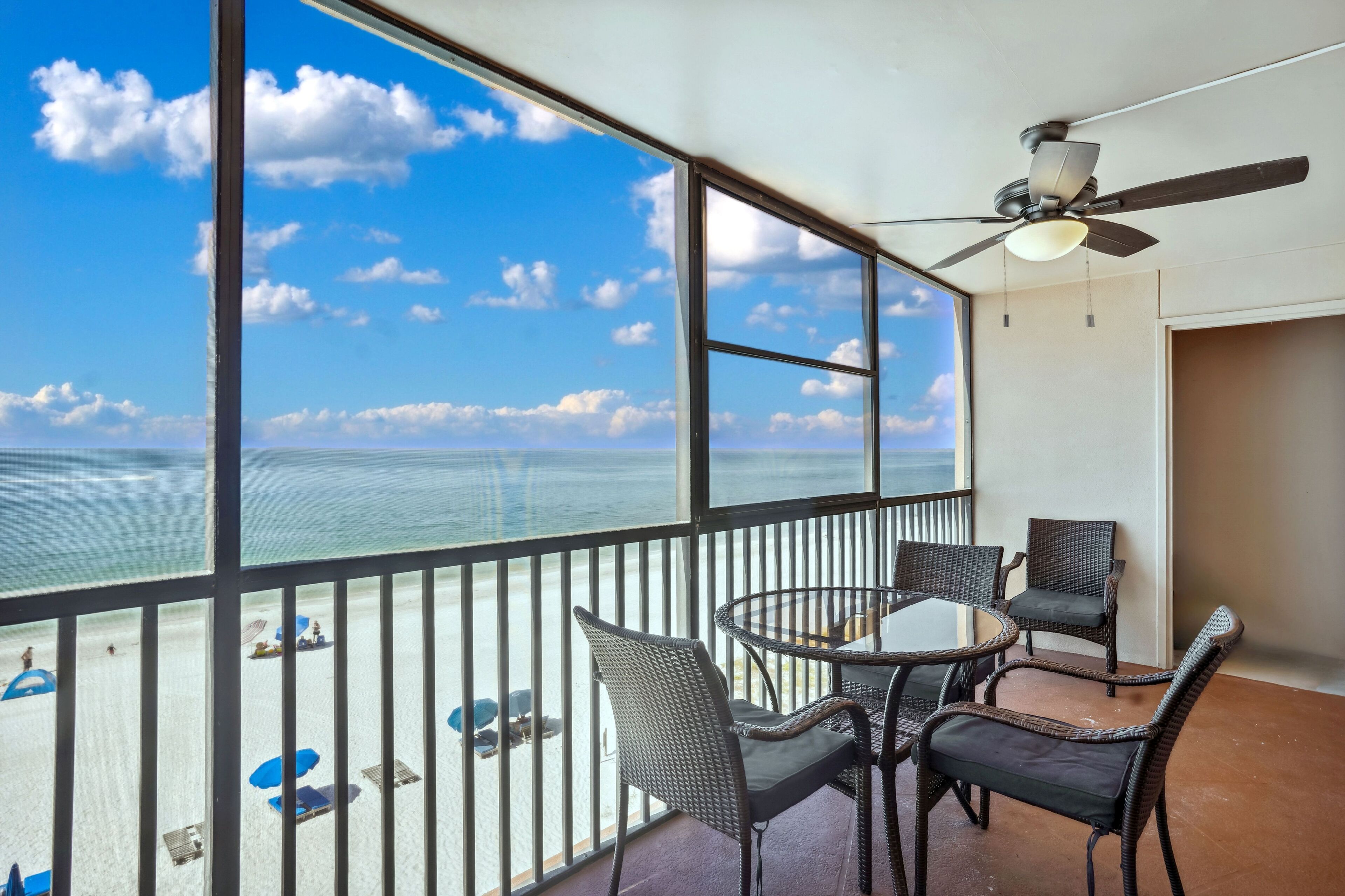 A balcony with a view of the ocean, wicker furniture, and a ceiling fan.