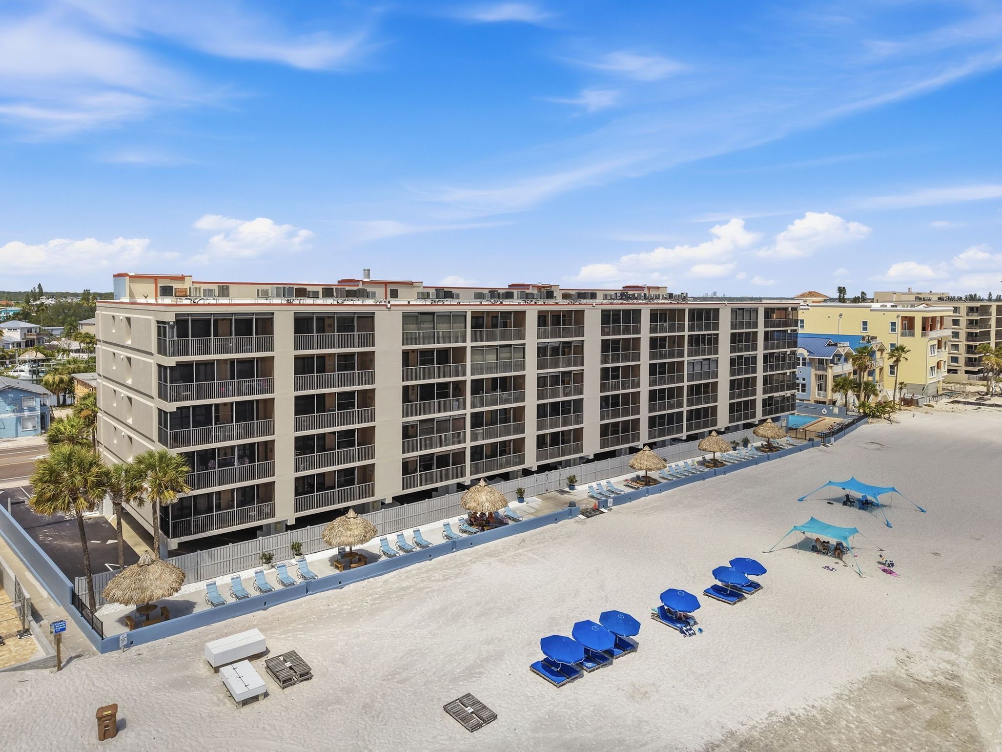 Un hôtel à plusieurs étages situé en bord de mer, doté de balcons, d’un espace piscine et de chaises longues.