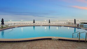 Une piscine avec vue sur la plage au coucher du soleil.