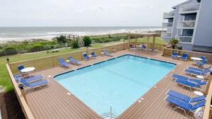 A pool area with lounge chairs and a view of the beach.