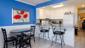 A kitchen with white cabinets, a blue wall, and a painting of red flowers.