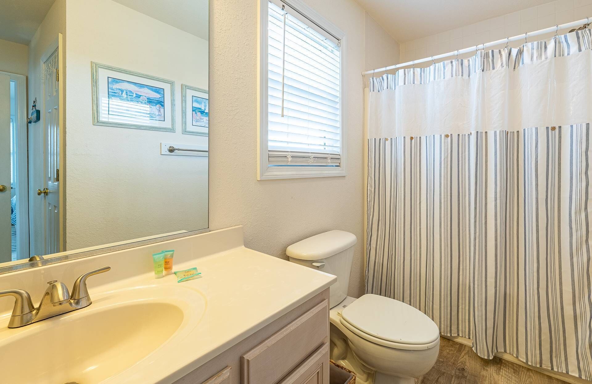 A bathroom with a sink, mirror, toilet, and window with blinds.