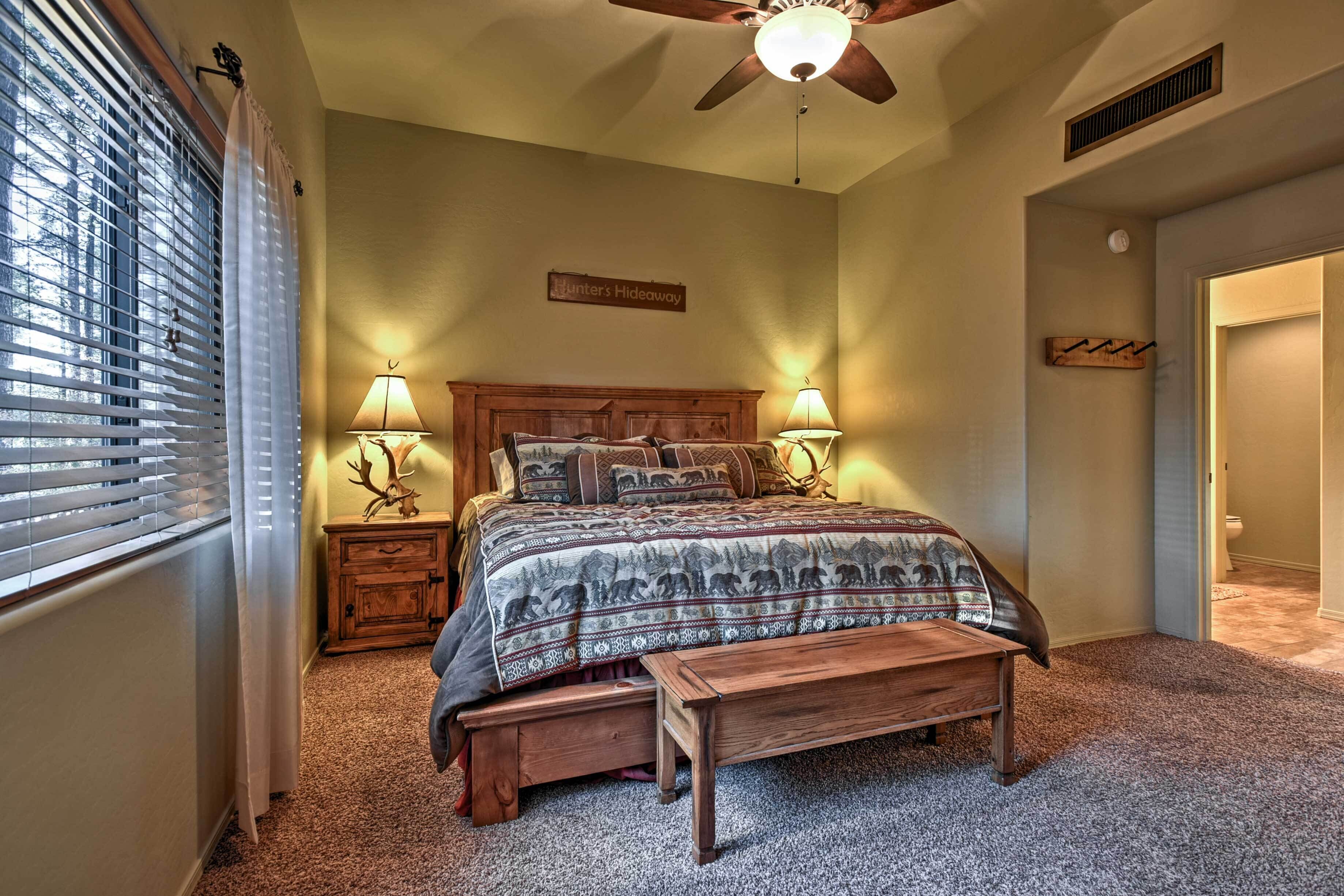 A bedroom with a bed, two bedside lamps, a wooden bench, a ceiling fan, and a sign on the wall.