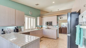A modern kitchen with light wood cabinets, a central island, a stainless steel refrigerator, and a microwave. - Heated Pool at 3 BR Home: 5 Mi to Coachella! (La Quinta)