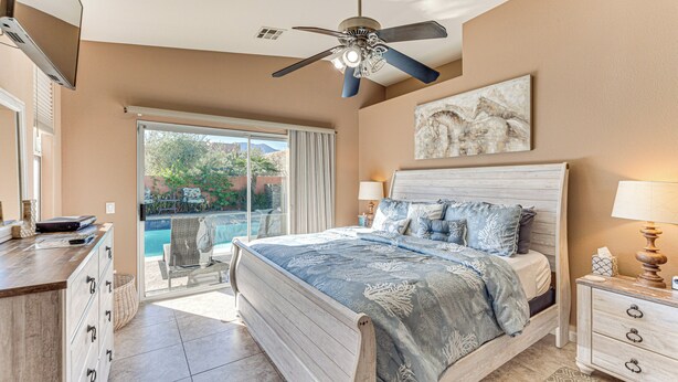 A bedroom with a bed, bedside tables, a ceiling fan, and a view of a swimming pool. - Heated Pool at 3 BR Home: 5 Mi to Coachella! (La Quinta)