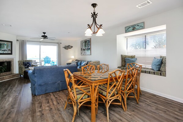 A dining area with a glass-top table and wicker chairs, a blue sofa, and a fireplace. - Great Gulf View, 2 Bedroom, Barrier Dunes 161-195 (Cape San Blas)