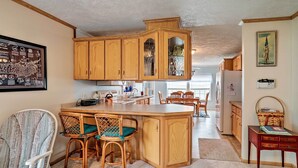 A kitchen with wooden cabinets, a central island, wicker chairs, and a dining table. - Lyndonville Home w/ Fire Pit, Screened Patio & A/C (Lyndonville)