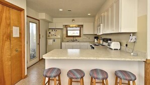 A kitchen with a central island, bar stools, white cabinets, and a wooden door. - OH1213- Just 300 Feet to Beach, 4 BRs, Ocean/Lighthouse Views, Dog Friendly! (Corolla)