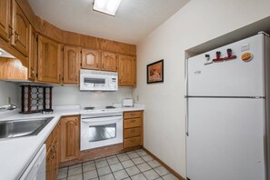 A kitchen with wooden cabinets, a white microwave, a stove, and a refrigerator.