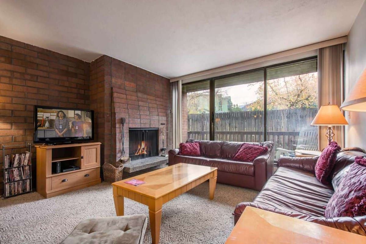 A living room with a fireplace, a television, and a large window.
