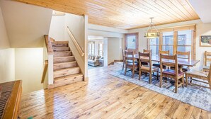 Una habitación amplia con suelos de madera, un comedor con sillas, una escalera y un techo con vigas de madera.