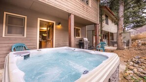 Un jacuzzi frente a una casa con porche, una parrilla y una silla.