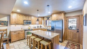 Una cocina con armarios de madera, un refrigerador de acero inoxidable, un microondas, una estufa y una encimera de granito.